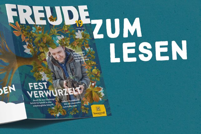 Die Freude Nr. 19 ist aufgeschlagen und liegt mit dem Cover nach oben. Sie zeigt quer liegend über die Vorder- und Rückseite einen Baum mit Wurzeln und Blättern, auf der Vorderseite ist au0erdem ein Mann, der Erde in der Hand hält. | © SONNENTOR