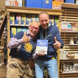 Am Foto ist Hannes mit einem Shopmitarbeiter oder Shopleiter abgebildet und hält das Buch "Wer spinnt, gewinnt" in der Hand, beide lachen in die Kamera. | © SONNENTOR