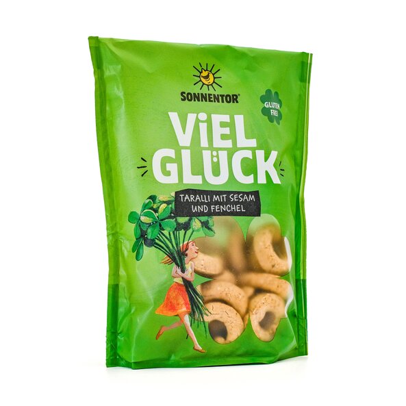SONNENTOR Viel Glück Taralli mit Sesam und Fenchel, grüne Packung mit Illustration einer jungen Frau mit großem Glücksklee und Sichtfenster. Im Sichtfenster ist das ringförmige, glutenfreie Knabbergebäck zu sehen.