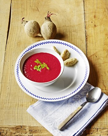 Auf dem Foto ist Rote-Rüben-Cremesuppe zu sehen. Daneben liegen Dinkelgrieß Nockerl auf dem Unterteller.  | © SONNENTOR