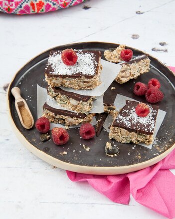 Auf dem Foto sind Brownies mit Schokoglasur zu sehen. Diese liegen schön angerichtet mit Himbeeren auf einem schwarzen Teller. | © SONNENTOR