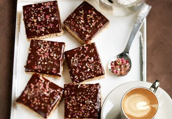 Auf dem Foto sind mehrere Stück Schokokuchen auf einem silbernen Tablett zu sehen. Der Kuchen ist mit Blüten dekoriert. | © SONNENTOR