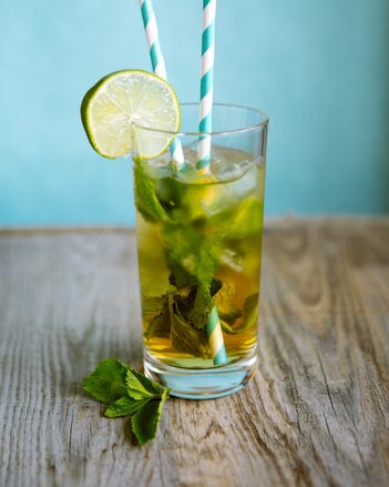 Auf dem Foto sieht man ein Glas mit Zitronen-Ingwer Eistee. Darin sind Minzblätter, Eiswürfel und Limettenscheiben zu sehen. | © SONNENTOR