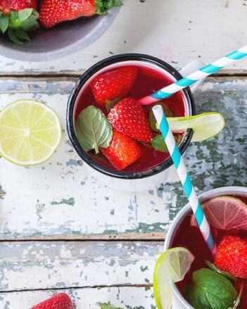 Auf dem Foto sind zwei Tassen mit roter Erdbeer Limonade zu sehen. Darin sind Erdbeeerstücke und Limettenscheiben zu sehen. | © SONNENTOR