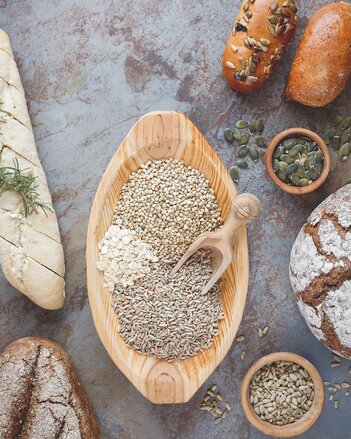 Auf dem Foto ist eine Holzschale mit diversen Körnern zu sehen. Auf dem Foto sind ebenfalls Weckerl, Brot und ein Gebäck zu sehen. | © SONNENTOR