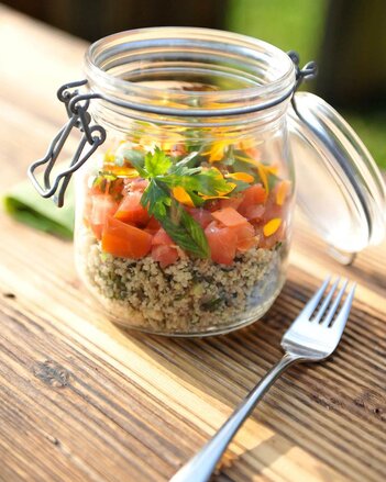 Foto von einem Glas Cous Cous Taboulé Salat auf einem Holztisch. Daneben liegt eine Gabel. | © SONNENTOR