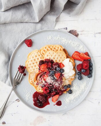 Auf dem Foto ist ein Teller mit Kokoswaffeln zu sehen. Wie sind mit Beeren und Kokosraspeln angerichtet. | © SONNENTOR