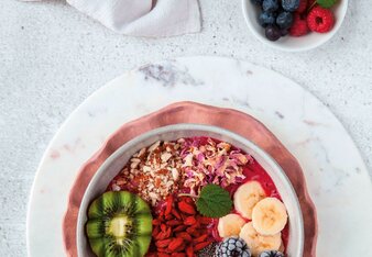 Auf dem Foto ist eine Acai Smoothie Bowl zu sehen. Diese ist mit frischen Kiwis, Beeren, Bananen und Blüten dekoriert.  | © SONNENTOR