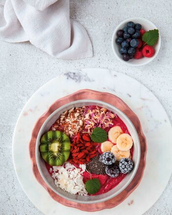 Auf dem Foto ist eine Acai Smoothie Bowl zu sehen. Diese ist mit frischen Kiwis, Beeren, Bananen und Blüten dekoriert.  | © SONNENTOR