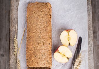 Auf dem Foto ist das Apfel-Kürbis-Brot zu sehen, daneben liegen Äpfel und Getreide. | © SONNENTOR