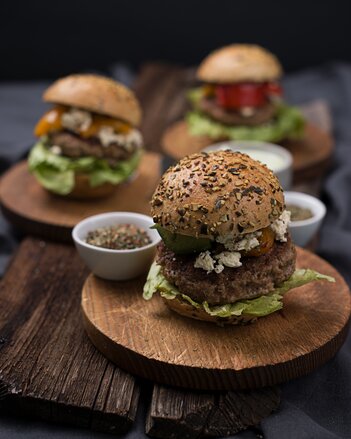 Auf dem Foto sind Burger Greek Style auf Holztellern zu sehen. Darauf steht auch eine kleine Schüssel mit Gewürzen. | © SONNENTOR