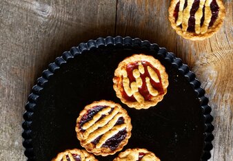 Foto von bunten Linzer-Tartalettes auf einem schwarzen Teller. | © SONNENTOR