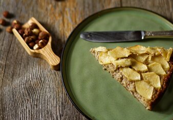 Auf dem Foto ist ein Stück Apfelkuchen zu sehen. Daneben sieht man Haselnüsse und im Hintergrund steht der restliche Kuchen. | © SONNENTOR