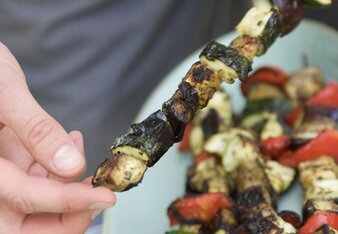 Auf dem Foto ist zu sehen, wie jemand einen Ratatouille-Spieß in der Hand hält. Auf einem Teller liegen noch weitere Spieße. | © SONNENTOR