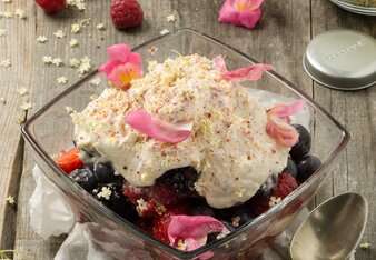 Foto von einer Schale mit Beeren-Blüten Salat. Darin sind verschiedenste Beeren mit weißer Creme und rosa Blüten zu sehen. | © SONNENTOR