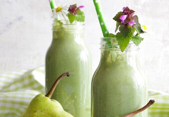 Auf dem Foto sind zwei große Gläser mit grünem Smoothie zu sehen. Davor sind halbe Birnen und Gänseblümchen zu sehen. | © SONNENTOR