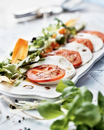 Auf dem Foto ist der Gute Laune Sommersalat mit Tomaten und Schafkäse zu sehen. Darauf sieht man das Kürbiskernöl und davor den Vogerlsalat. | © SONNENTOR