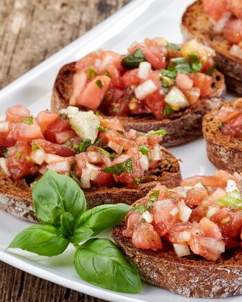 Auf dem Foto sind mehrere Glück Bruschetta zu sehen. Davor sind Basilikumblätter zu sehen. | © SONNENTOR