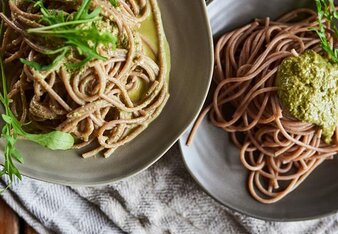 Auf dem Foto sind zwei Teller mit Buchweizennudeln mit Pesto zu sehen. Die Nudeln sind mit Rucola garniert. | © SONNENTOR