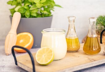 Auf dem Foto ist ein Tablett mit einem Glas Joghurtdressing zu sehen. Daneben sieht man eine halbe Limette und Orange, sowie zwei kleine Kännchen. | © SONNENTOR