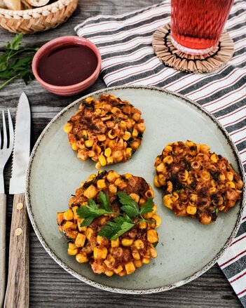 Drei Corn Fritters liegen auf einem Teller, dekoriert mit Petersilie. | © SONNENTOR