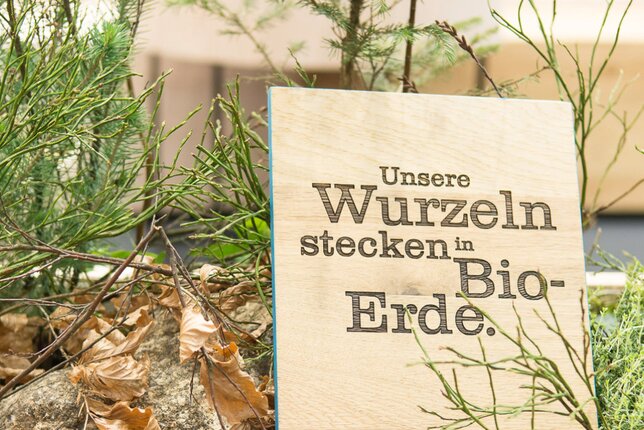 Auf dem Foto ist eine Holztafel zu sehen. Darauf stehen die Worte - Unsere Wurzeln stecken in Bio-Erde. | © SONNENTOR