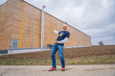 Auf dem Foto steht Hannes vor der neuen Halle Himmelhoch und deutet mit den Armen darauf.  | © SONNENTOR