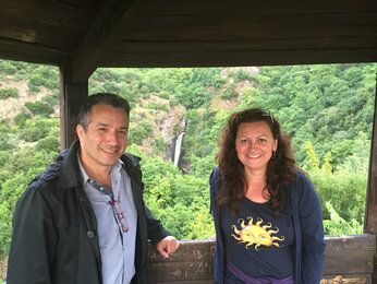 Foto von zwei Personen in der Natur in Griechenland. Im Hintergrund ist ein Wasserfall zu sehen. | © SONNENTOR