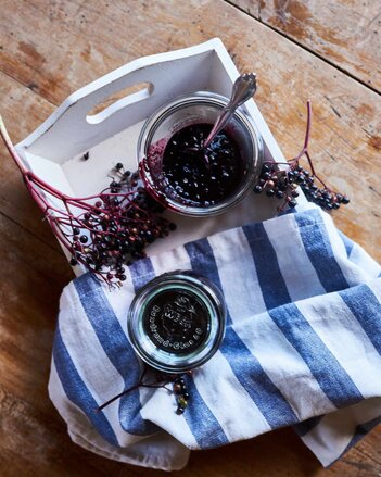 Auf dem Foto sieht man ein Glas mit Hollerkoch. Daneben sieht man frische Hollunderbeeren. | © SONNENTOR