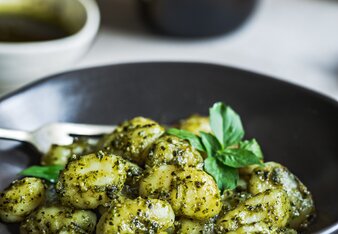 Auf dem Foto ist ein schwarzer Teller mit Gnocchi mit Kräuterpesto zu sehen. Im Hintergrund sieht man ein Schälchen mit dem Pesto. | © SONNENTOR