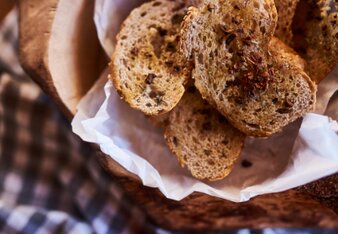 Auf dem Foto sind Brotchips mit Tomatenflocken-Öl in einem Körbchen zu sehen. Dahinter sieht man Tomaten. | © SONNENTOR