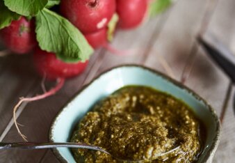 Auf dem Foto ist ein Schälchen mit Radieschengrün-Pesto zu sehen. Dahinter sind frische Radieschen zu sehen. | © SONNENTOR