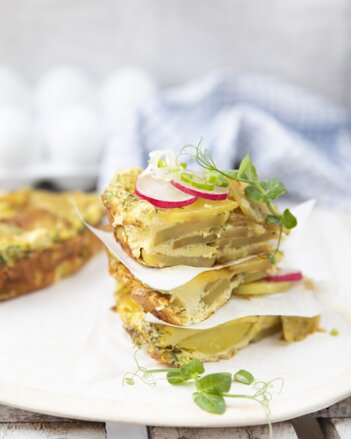 Auf dem Foto sieht man einen Turm aus Tortillas de Patatas. Sie sind mit Radieschen, Jungzwiebel und Sprossen garniert. | © SONNENTOR