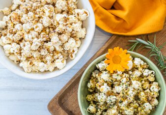 Auf dem Foto sind zwei Schüsseln mit Gewürzblüten Popcorn zu sehen. Darin ist auch eine orangene Blüte und ein Rosmarinzweig zu sehen. | © SONNENTOR