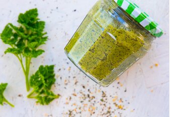 Auf dem Foto ist ein Glas mit Petersilien-Pesto zu sehen. Daneben sind Gewürze verstreut und auch frische Petersilie ist neben dem Glas zu sehen. | © SONNENTOR