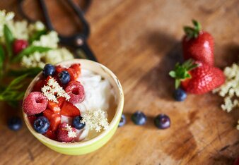 Auf dem Foto sieht man eine Schale mit Joghurt garniert mit bunten Beeren und Holunderblüten. | © SONNENTOR