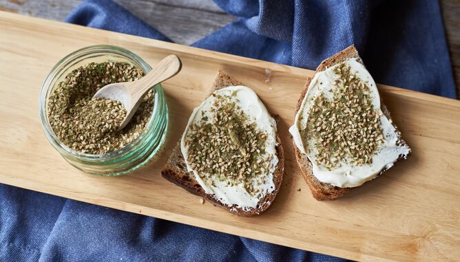 Auf dem Foto sieht man Brot mit Aufstrich und Zatar darauf. Daneben steht ebenfalls ein Glas mit Zatar. | © SONNENTOR