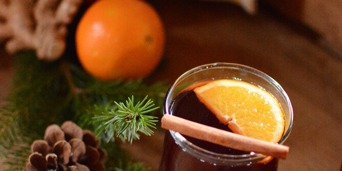 Auf dem Foto sieht man ein Glas mit Kaminknistern Punsch. Darin sieht man eine Orangenscheibe und eine Zimtstange. | © SONNENTOR